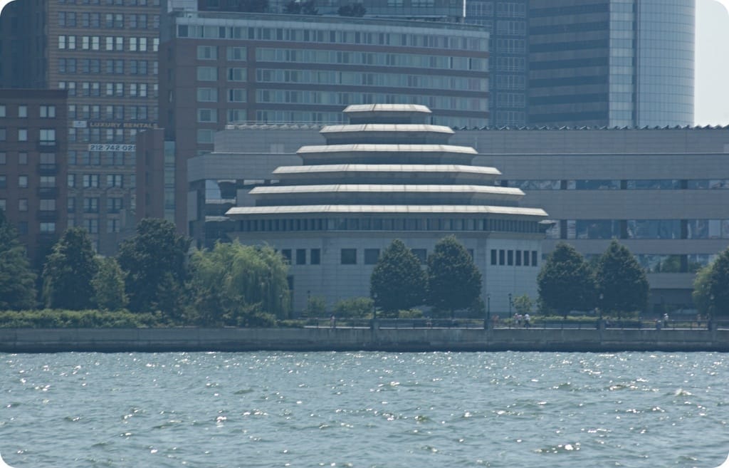Edificio del Museum of Jewish Heritage con il suo caratteristico tetto a gradoni, affacciato sul lungofiume e circondato dai grattacieli di Manhattan e un viale alberato.