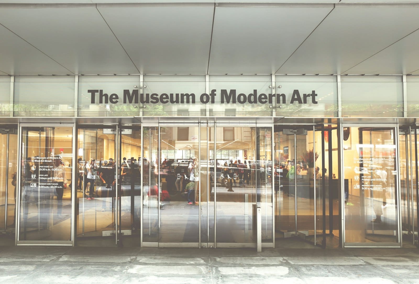 Ingresso in vetro del The Museum of Modern Art con visitatori che entrano nella luminosa hall e il nome del museo sopra le porte.