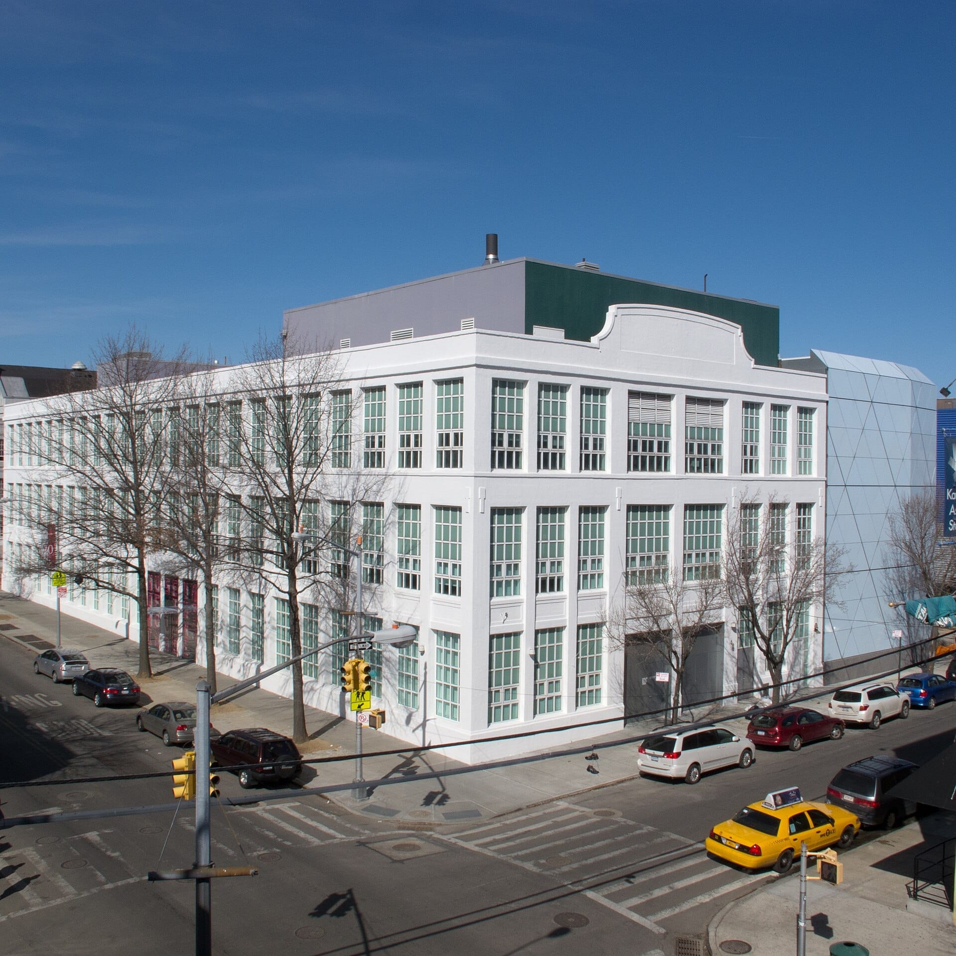 L'edificio bianco con finestre del Museum of the Moving Image su un angolo della città ad Astoria, con auto e alberi spogli che costeggiano la strada.