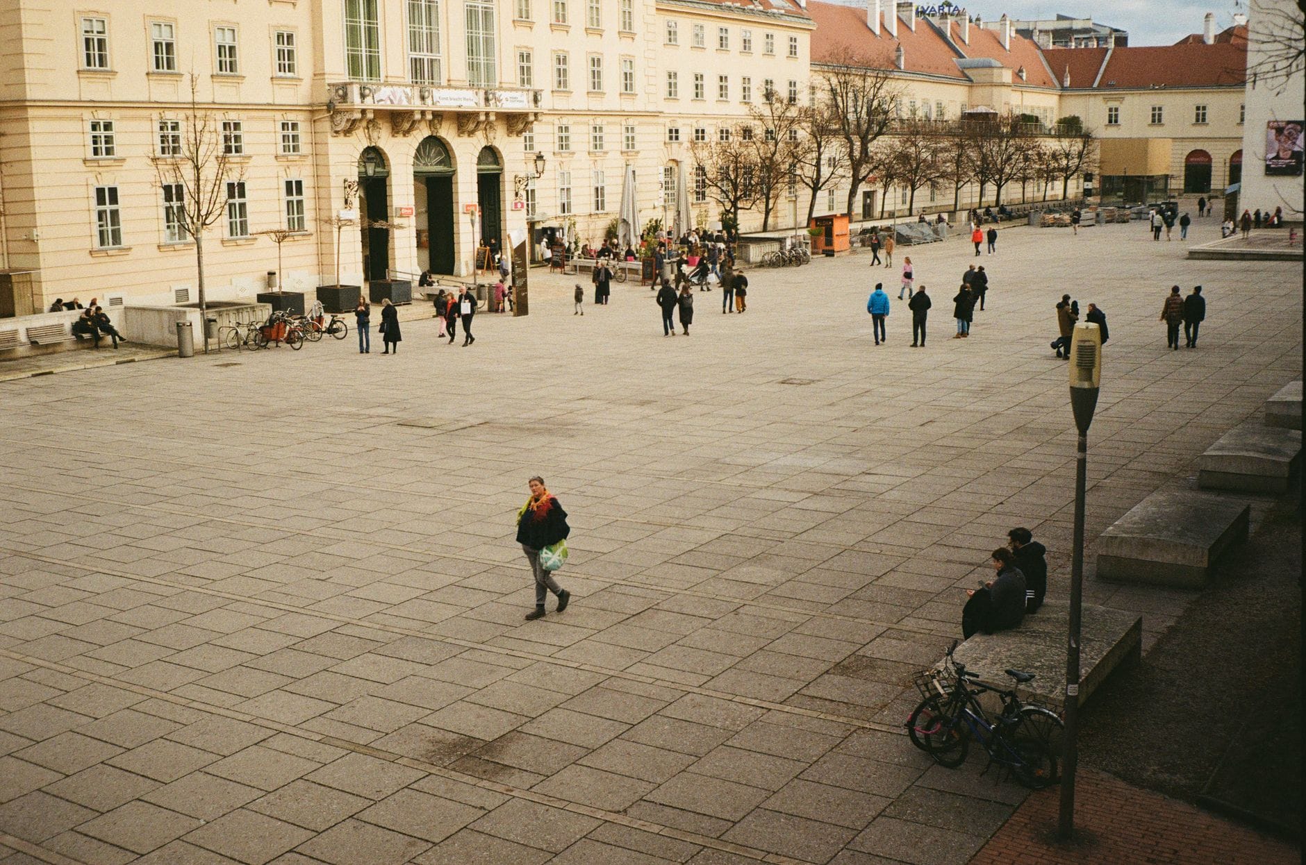 Weitläufiger, öffentlicher Innenhof des MuseumsQuartiers in Wien mit Menschen, die spazieren, sitzen und den Kulturkomplex inmitten historischer Gebäude genießen.