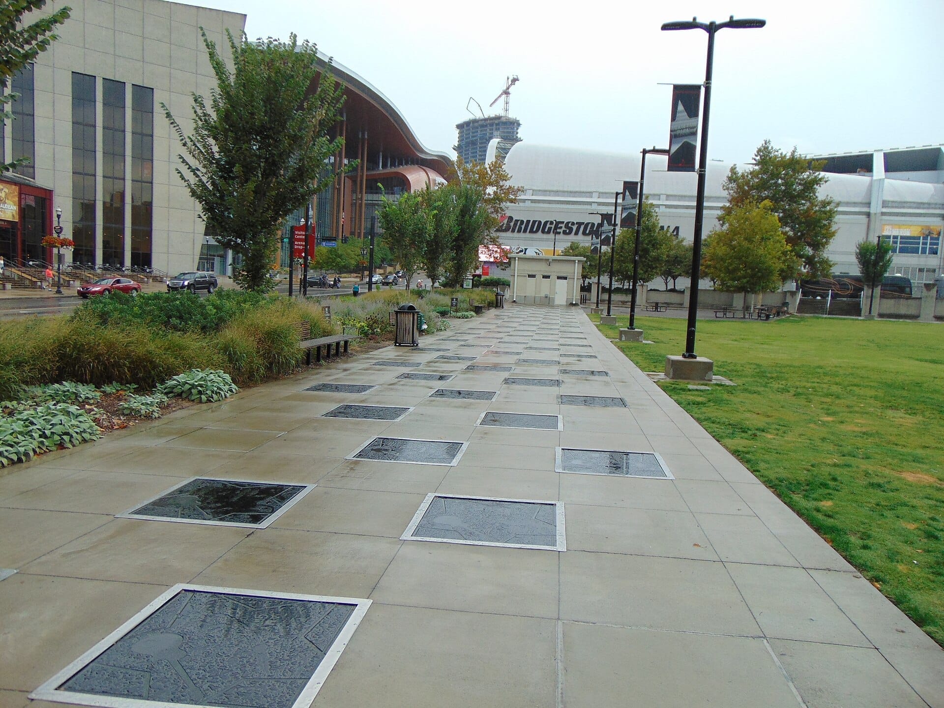 Paseo de concreto bordeado de placas con nombres en el Music City Walk of Fame Park en el centro de Nashville, con edificios modernos y vegetación en un día nublado.