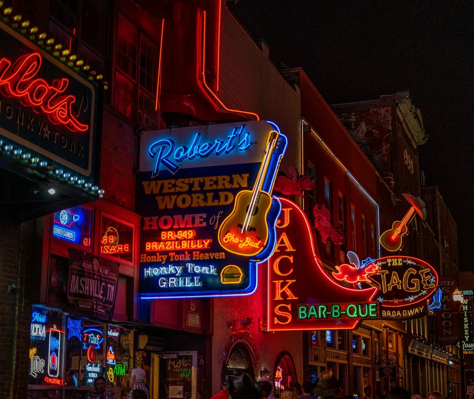Coloridos letreros de neón de Roberts Western World y Jacks Bar-B-Que iluminan Music Row de Nashville por la noche, atrayendo visitantes a los animados honky tonks.