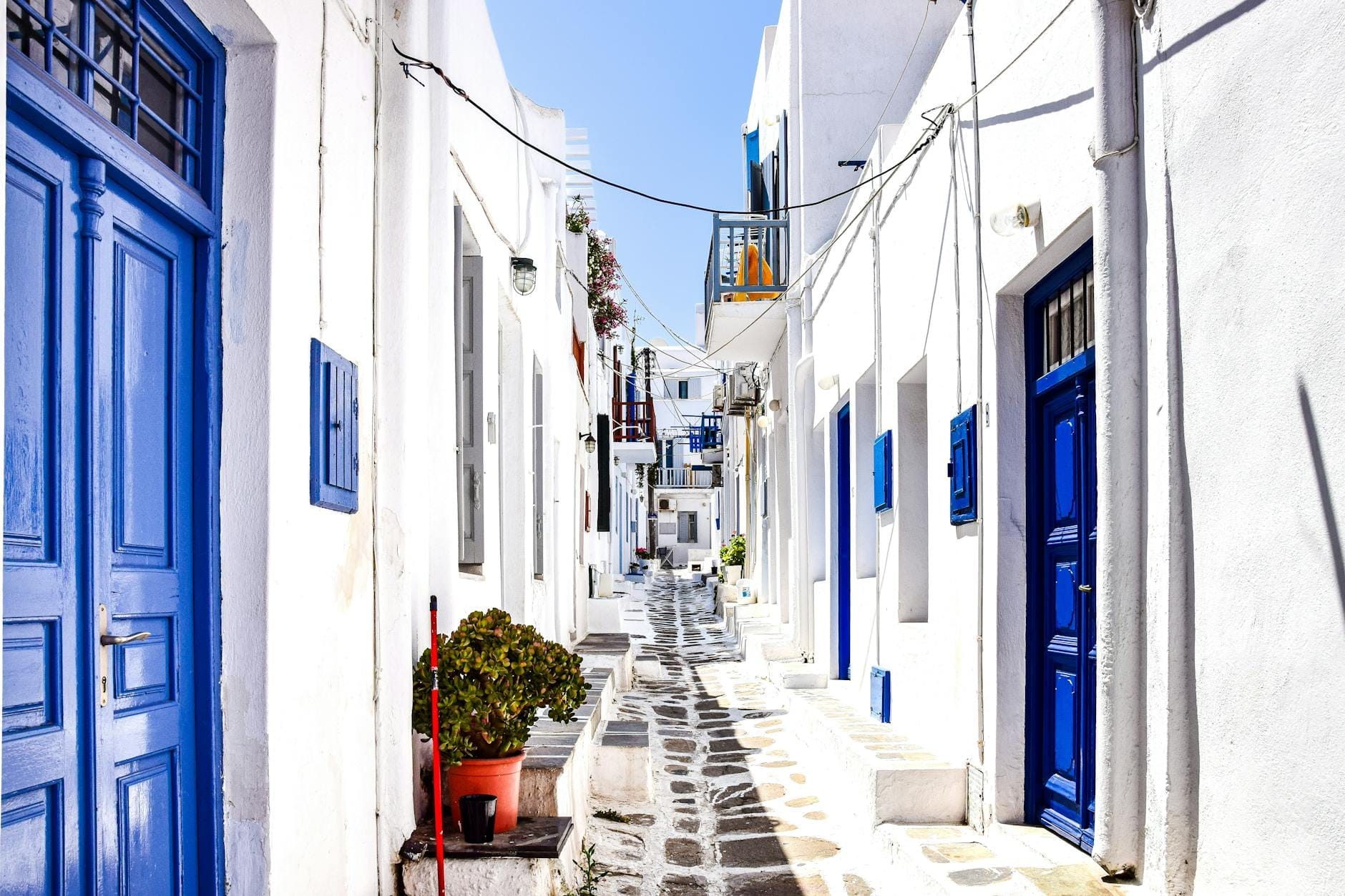 Callejón de piedra luminoso y soleado en el casco antiguo de Mykonos con edificios blancos tradicionales y puertas azules, perfecto para un paseo pintoresco.