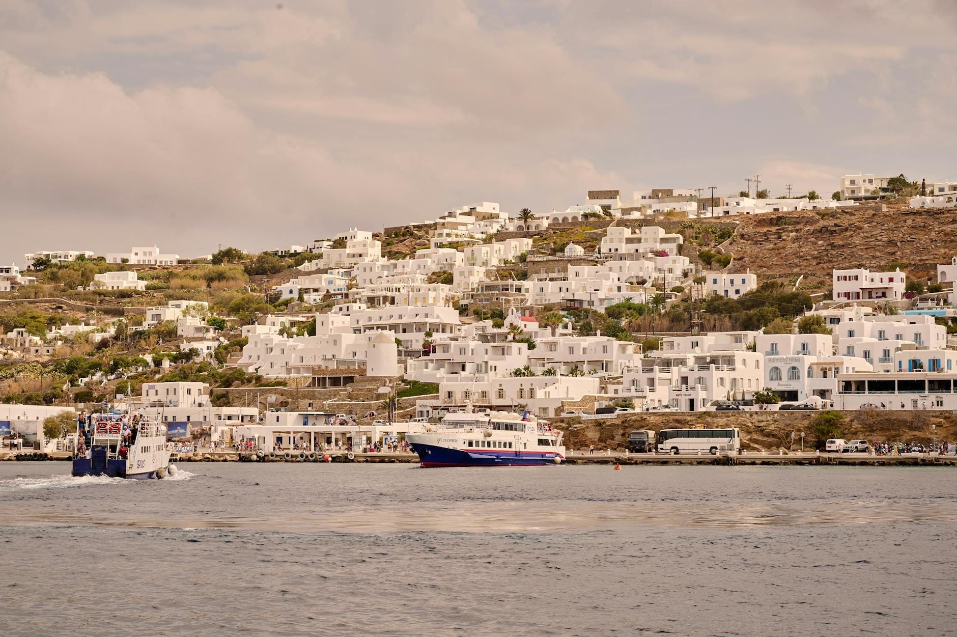 Ferrys y catamaranes atracados en el Puerto Nuevo de Mykonos con edificios encalados que se elevan por la ladera detrás.