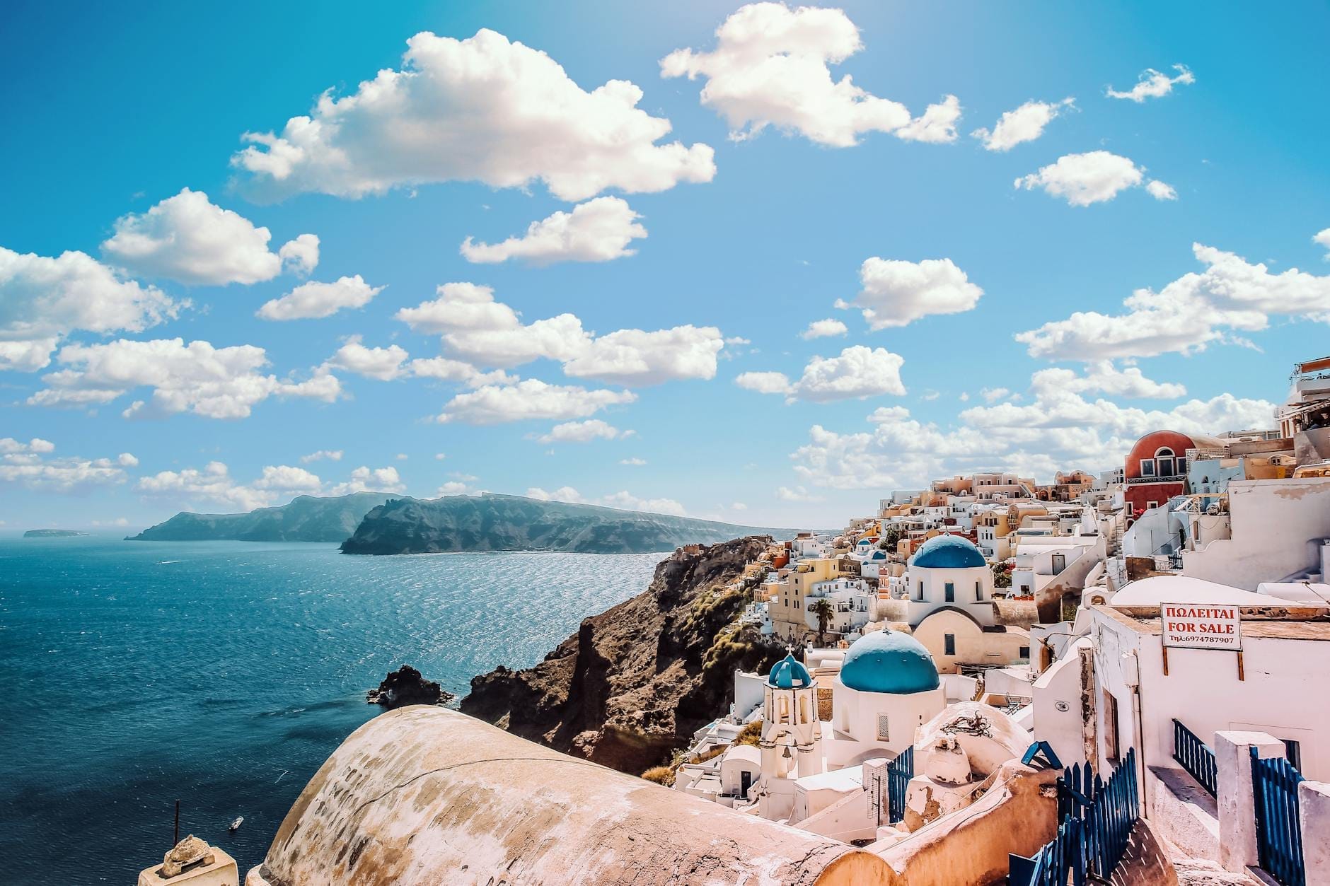 Vista panorámica impresionante de Santorini con sus icónicas iglesias de cúpula azul, edificios blancos y acantilados dramáticos sobre el brillante mar Egeo en un día soleado.