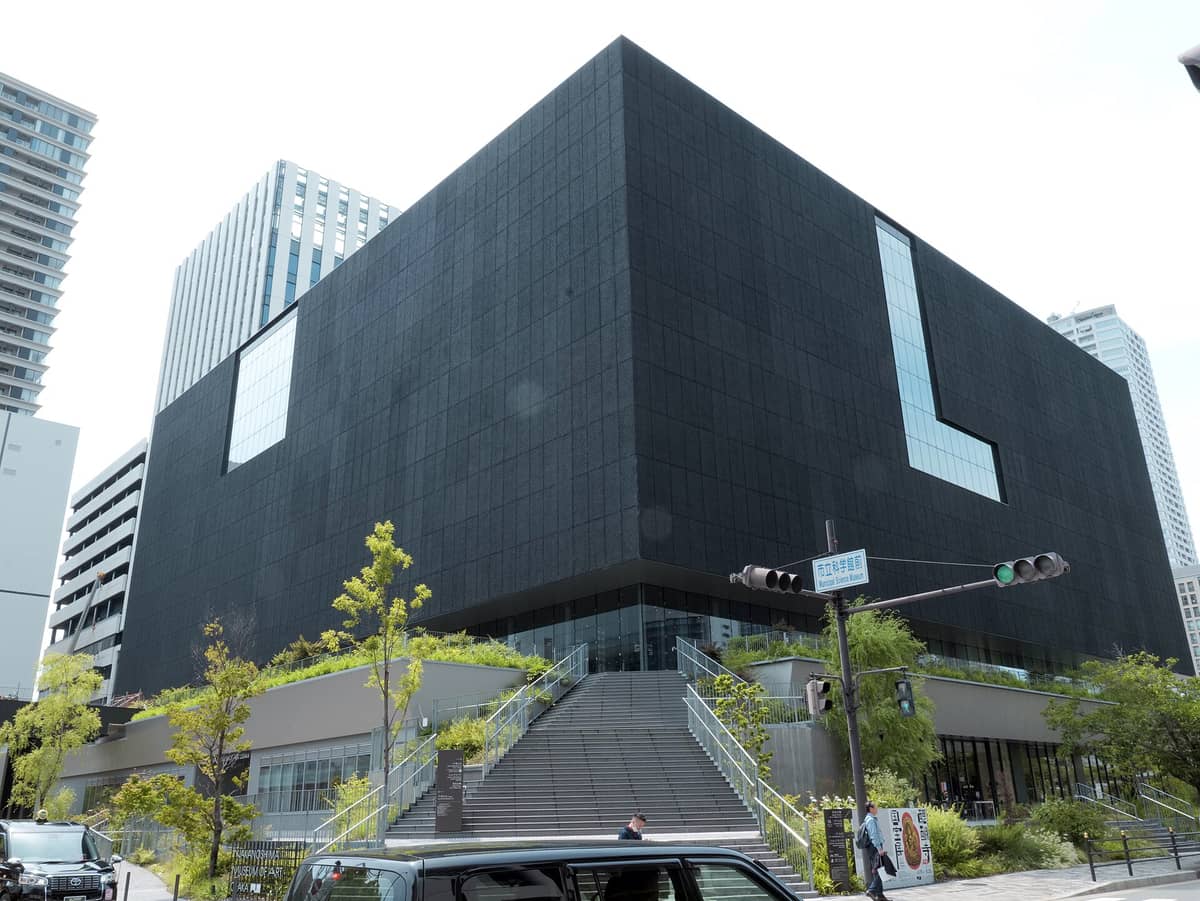 Exterior view of the bold matte-black cube building of the Nakanoshima Museum of Art Osaka, with wide steps and modern urban surroundings.
