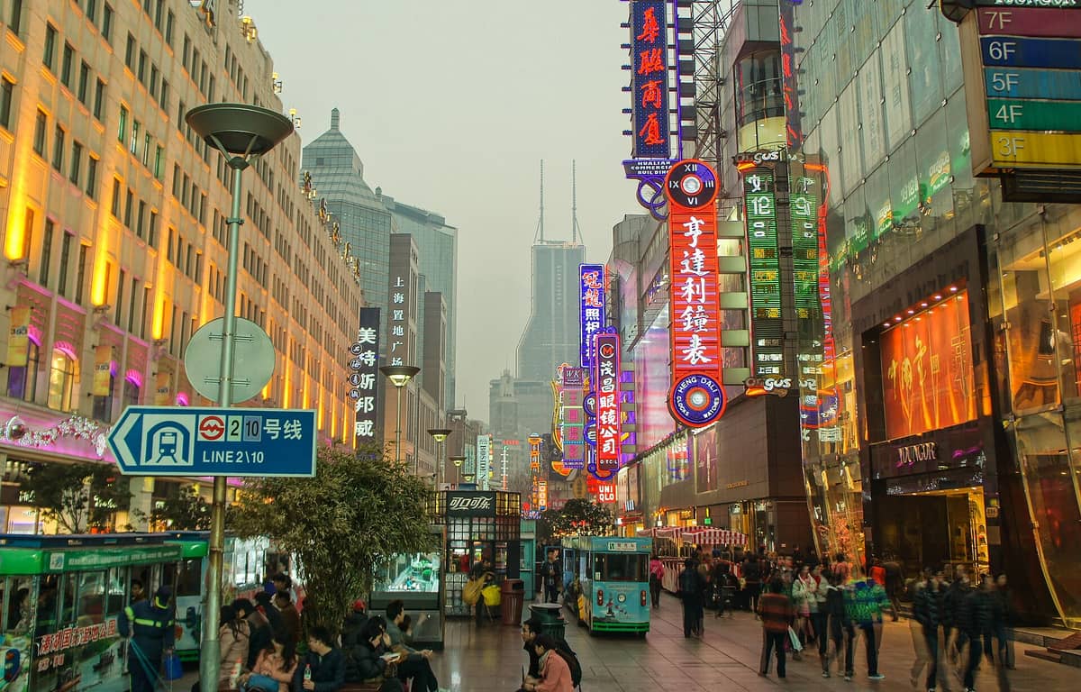Weitläufiger, farbenprächtiger Blick auf die Nanjing Road Fußgängerzone in Shanghai mit Leuchtreklamen, belebten Menschenmassen, Geschäften und Hochhäusern.