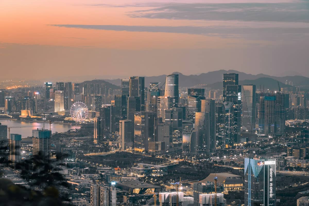 Vista panorâmica do distrito de Nanshan, em Shenzhen, ao pôr do sol, com o skyline moderno de arranha-céus, orla marítima e uma grande roda-gigante.