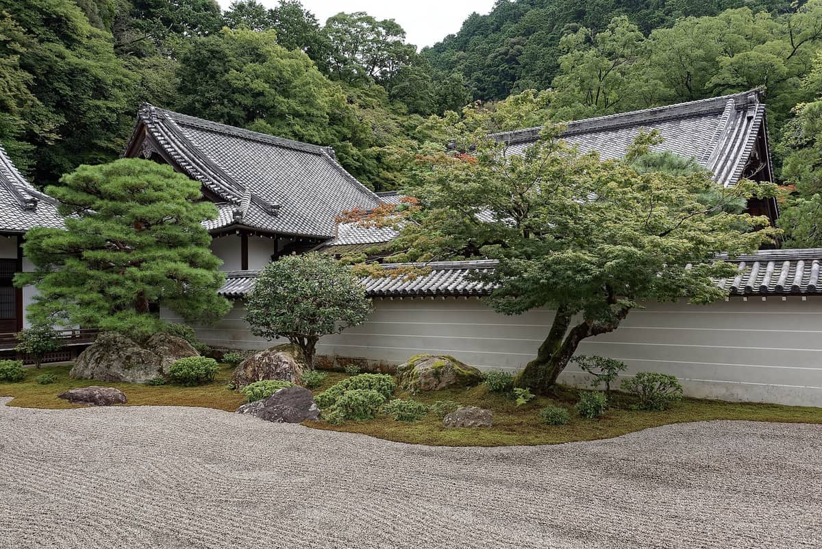 Traditional wooden rooftops and serene Zen garden at Nanzen-ji Temple, bordered by lush greenery and raked gravel in Kyoto, Japan.