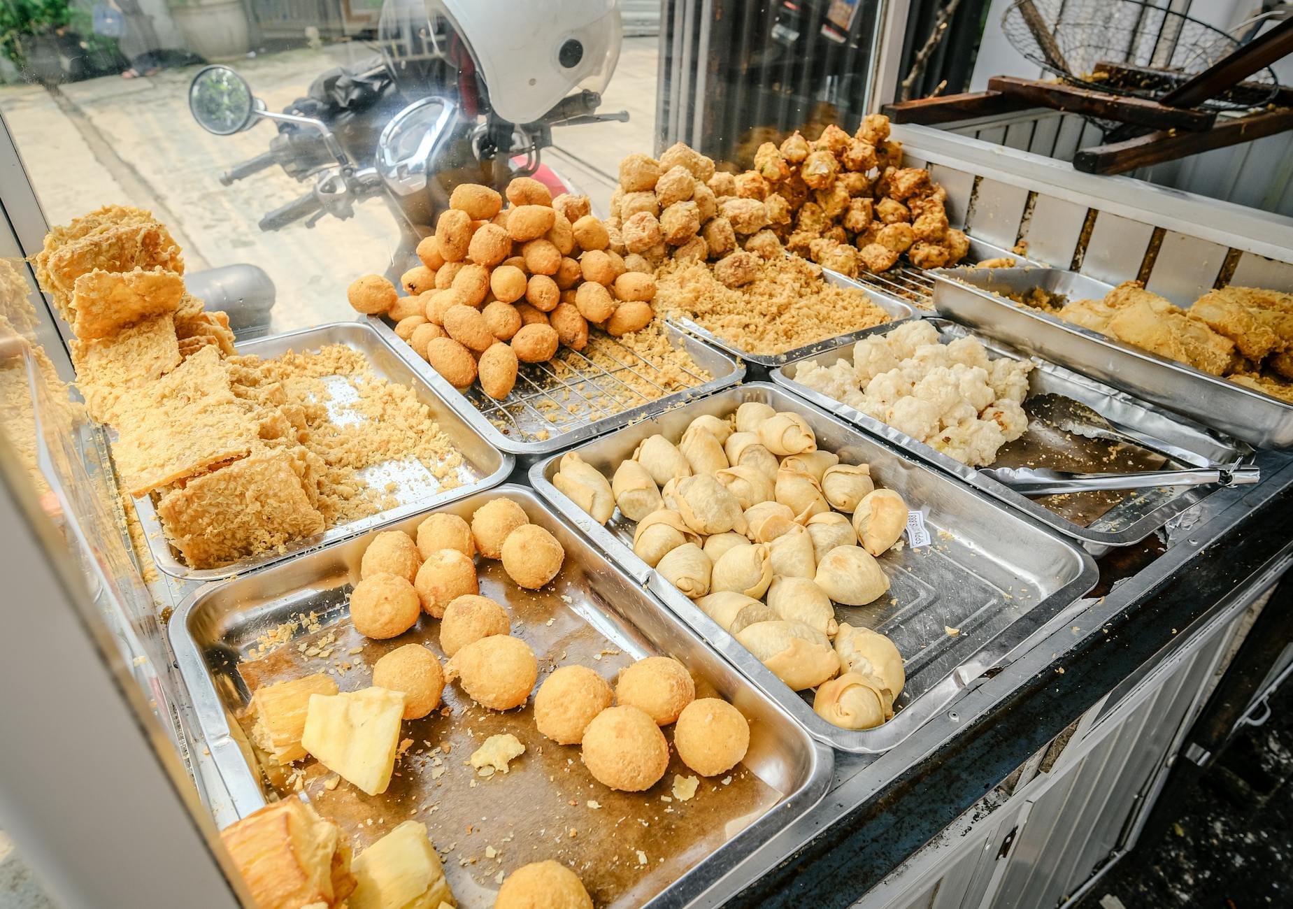 Gros plan d'un stand de street food à Naples présentant des plateaux de snacks frits assortis comme des arancini et des crocche sur un trottoir animé.