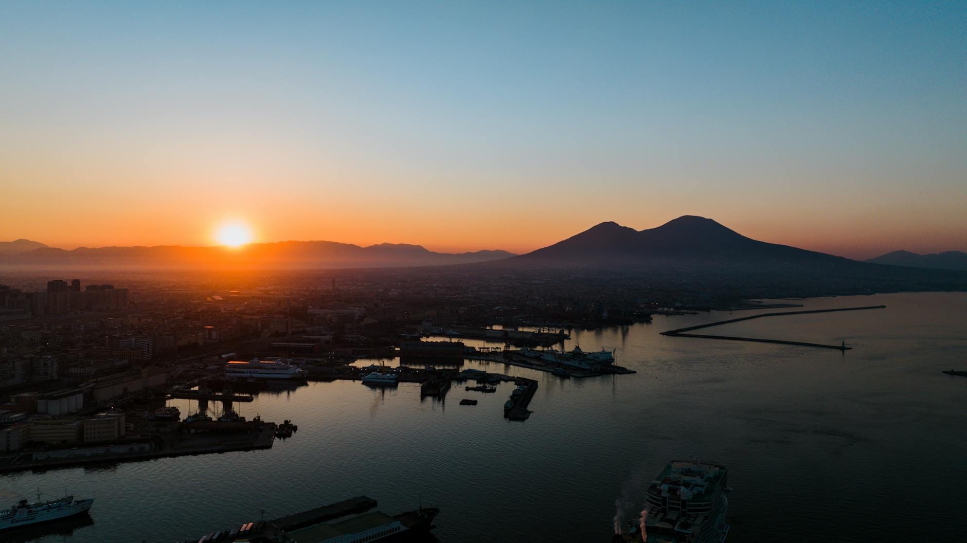 Vue aérienne sur le golfe de Naples au coucher du soleil avec le Vésuve en arrière-plan et les bâtiments de la ville le long du front de mer.