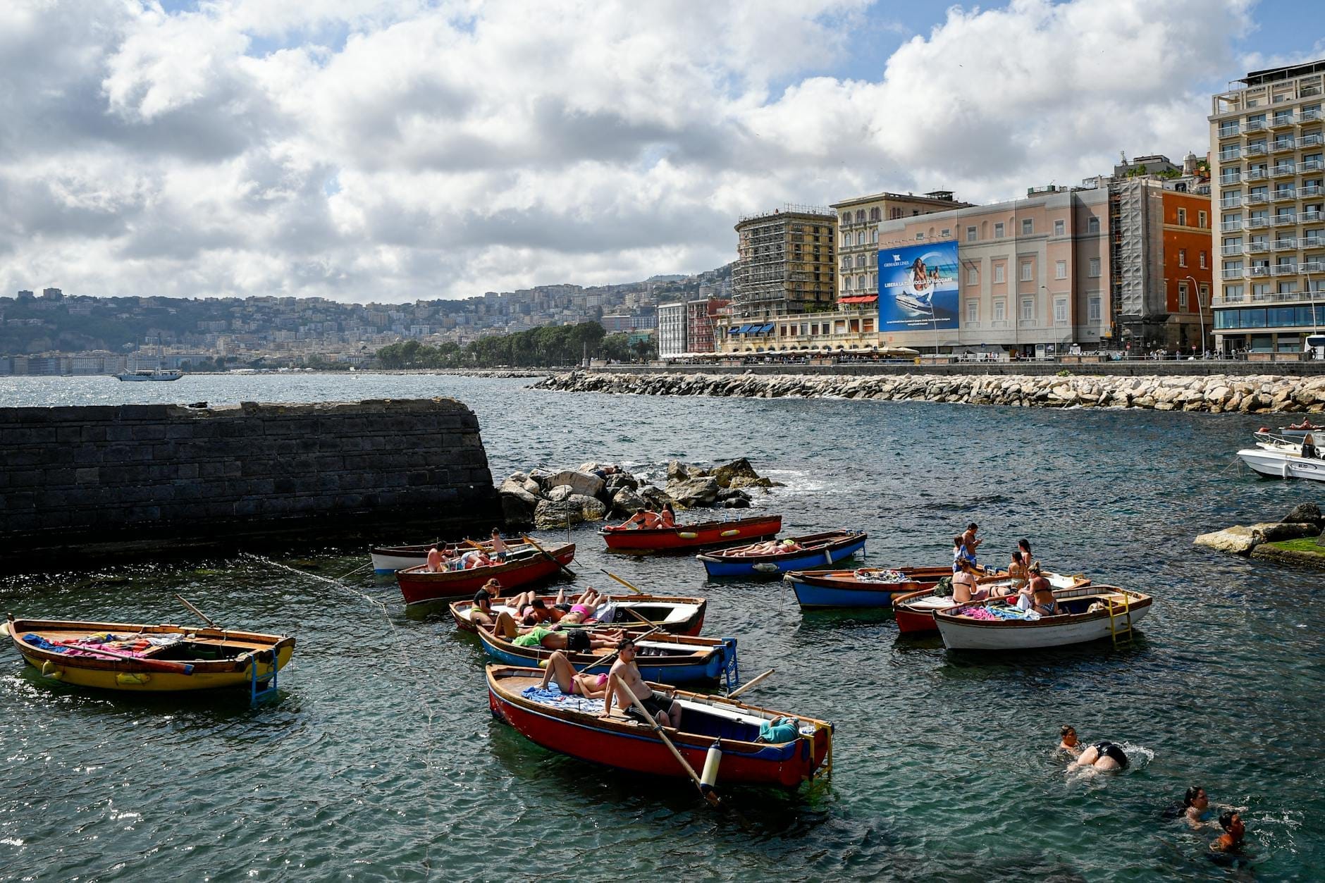 Bateaux colorés sur le front de mer de Naples avec d'élégants hôtels et bâtiments longeant la promenade en bord de mer.