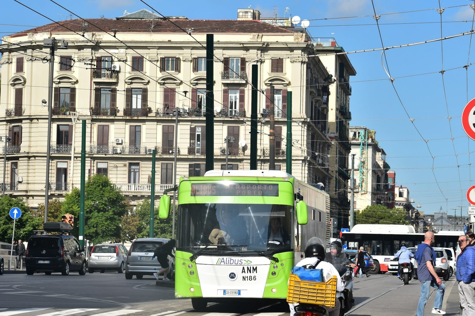 Ônibus de traslado para o aeroporto Alibus no centro de Nápoles com edifícios e pessoas por perto em um dia ensolarado