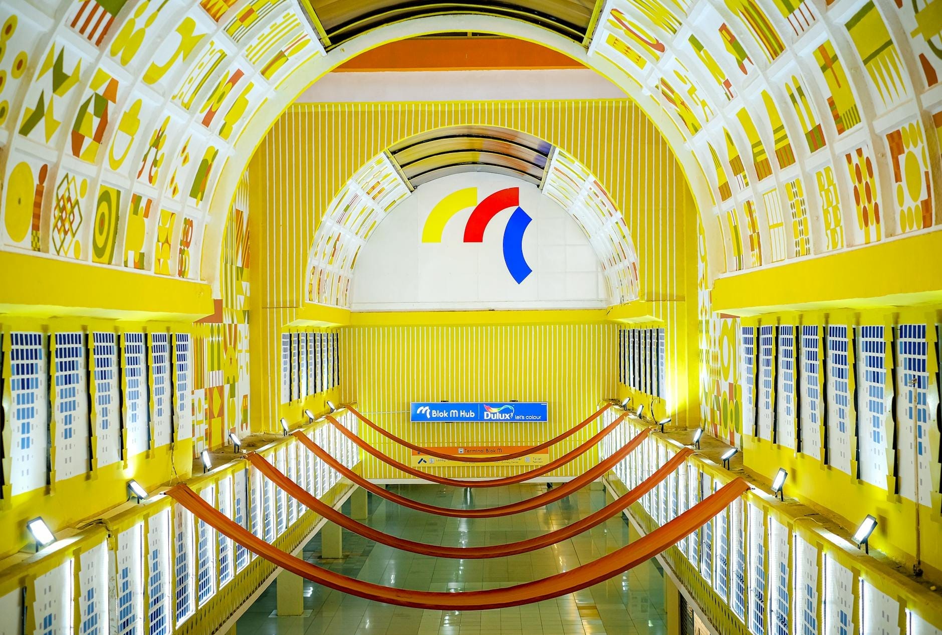 Estação de metrô de Nápoles bem iluminada com decoração amarela, arcos artísticos e uma placa azul da estação com o nome 'Dante' acima da plataforma.