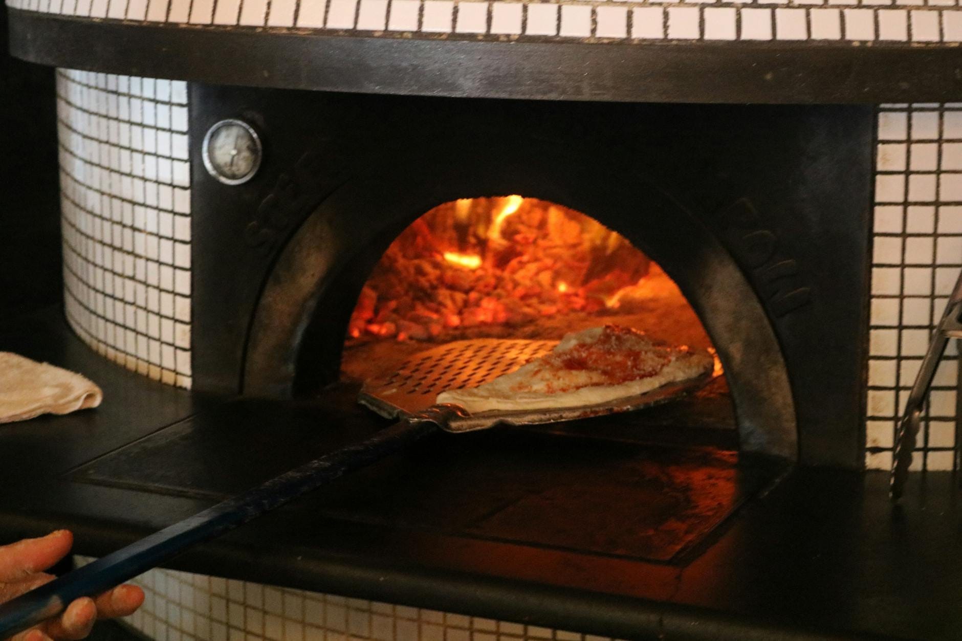 Une pizza placée dans un four à bois traditionnel avec des braises ardentes, illustrant la technique de fabrication de la pizza napolitaine.