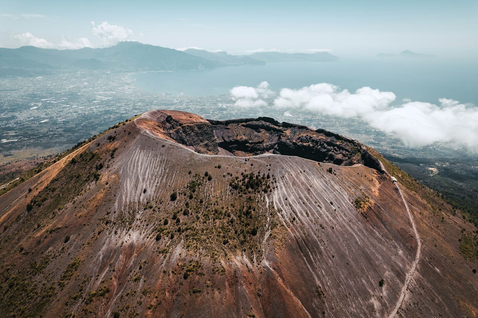 Vue aérienne directement au-dessus du cratère spectaculaire du Mont Vésuve avec la côte de Naples et la mer bleue en arrière-plan.