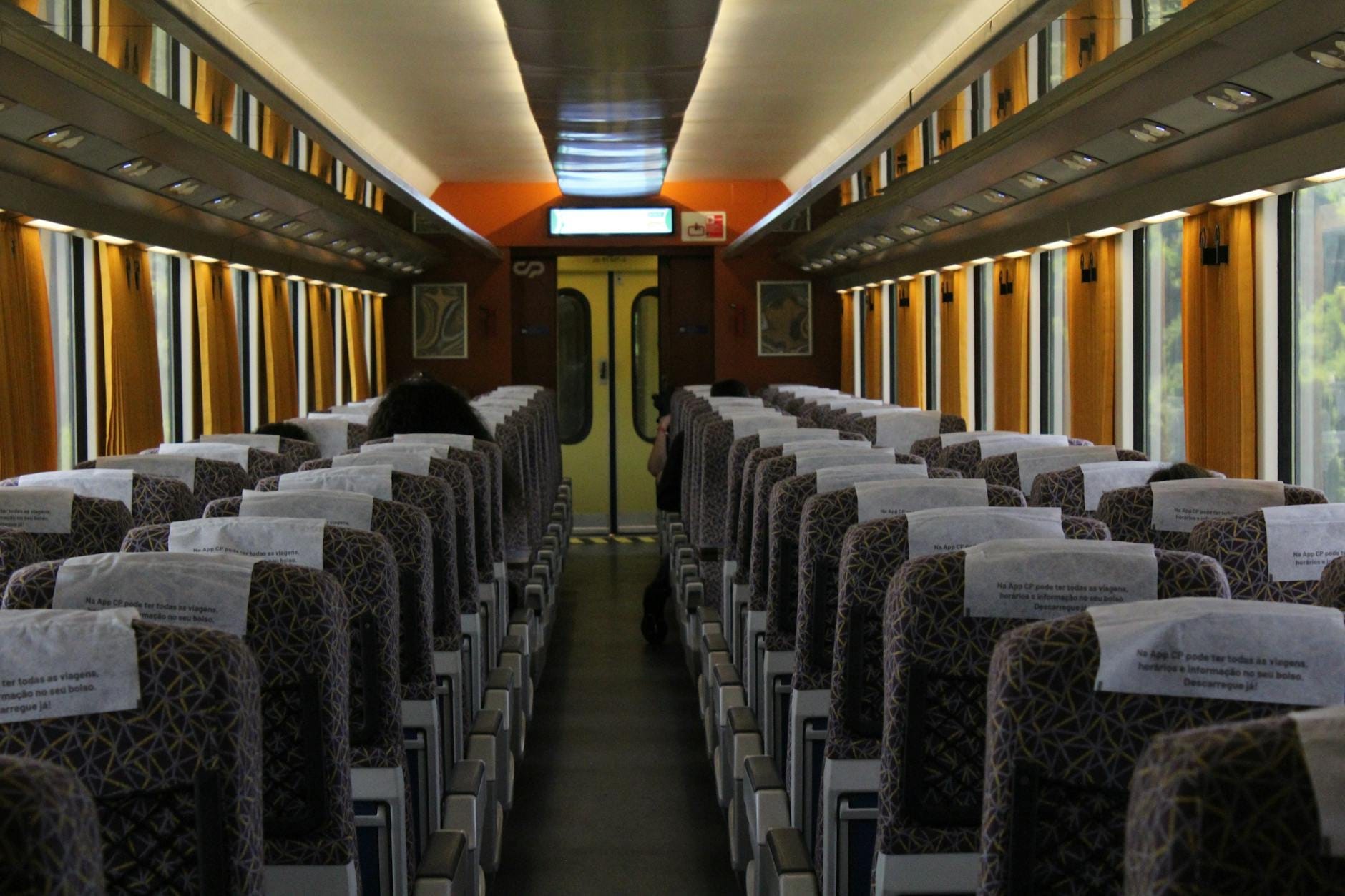 Intérieur lumineux d'un wagon de train avec des rangées de sièges à motifs et des accents orange, évoquant un voyage en train régional italien.