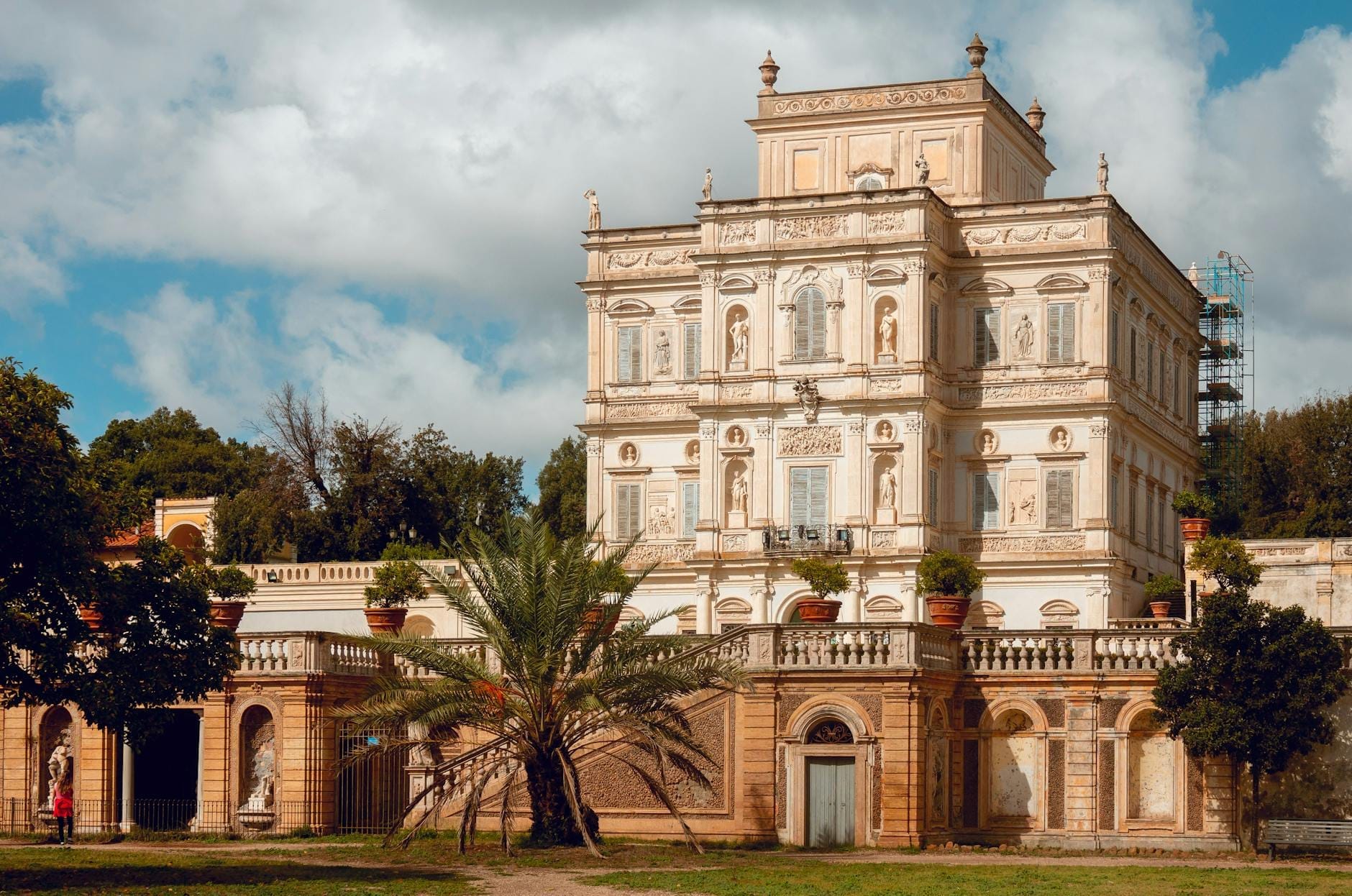Grande villa histórica rodeada por um amplo parque verde com árvores em Nápoles sob um céu azul.