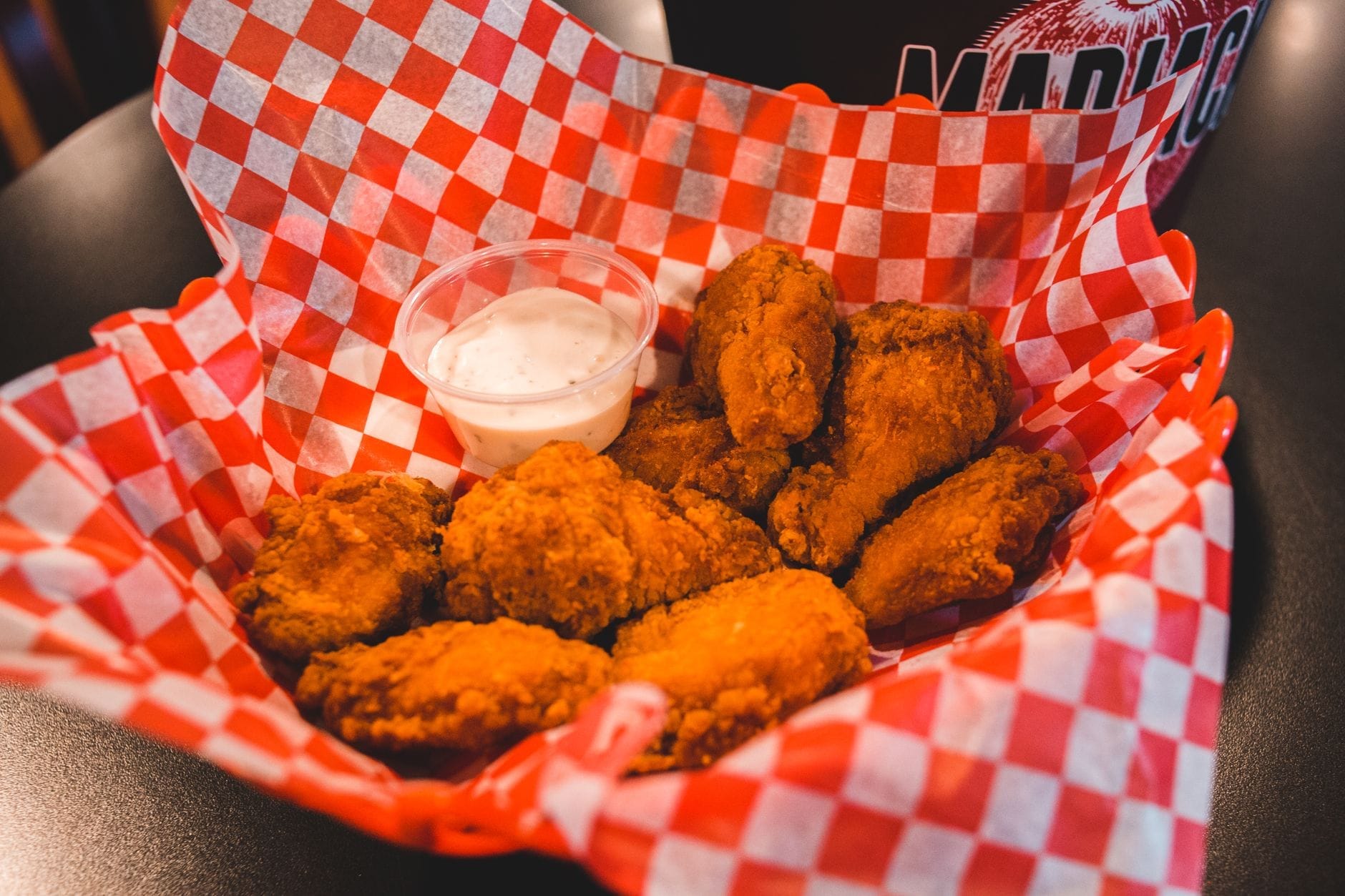Una cesta de alitas de pollo picantes estilo Nashville con salsa para mojar sobre un mantel a cuadros rojos en una mesa de restaurante.