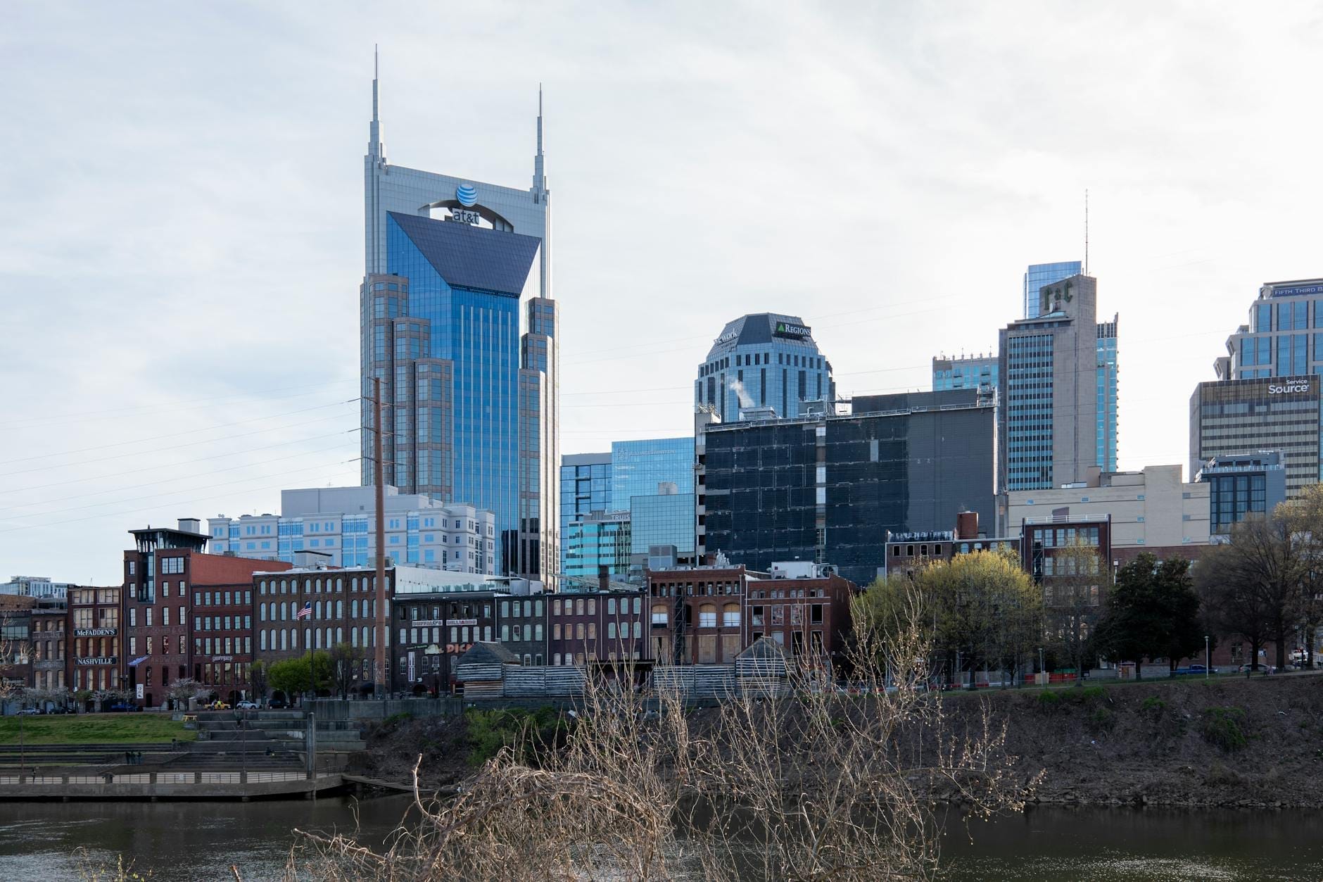 Vista diurna del horizonte de Nashville con el icónico edificio AT&T, hoteles modernos y estructuras de ladrillo a lo largo del paseo fluvial.