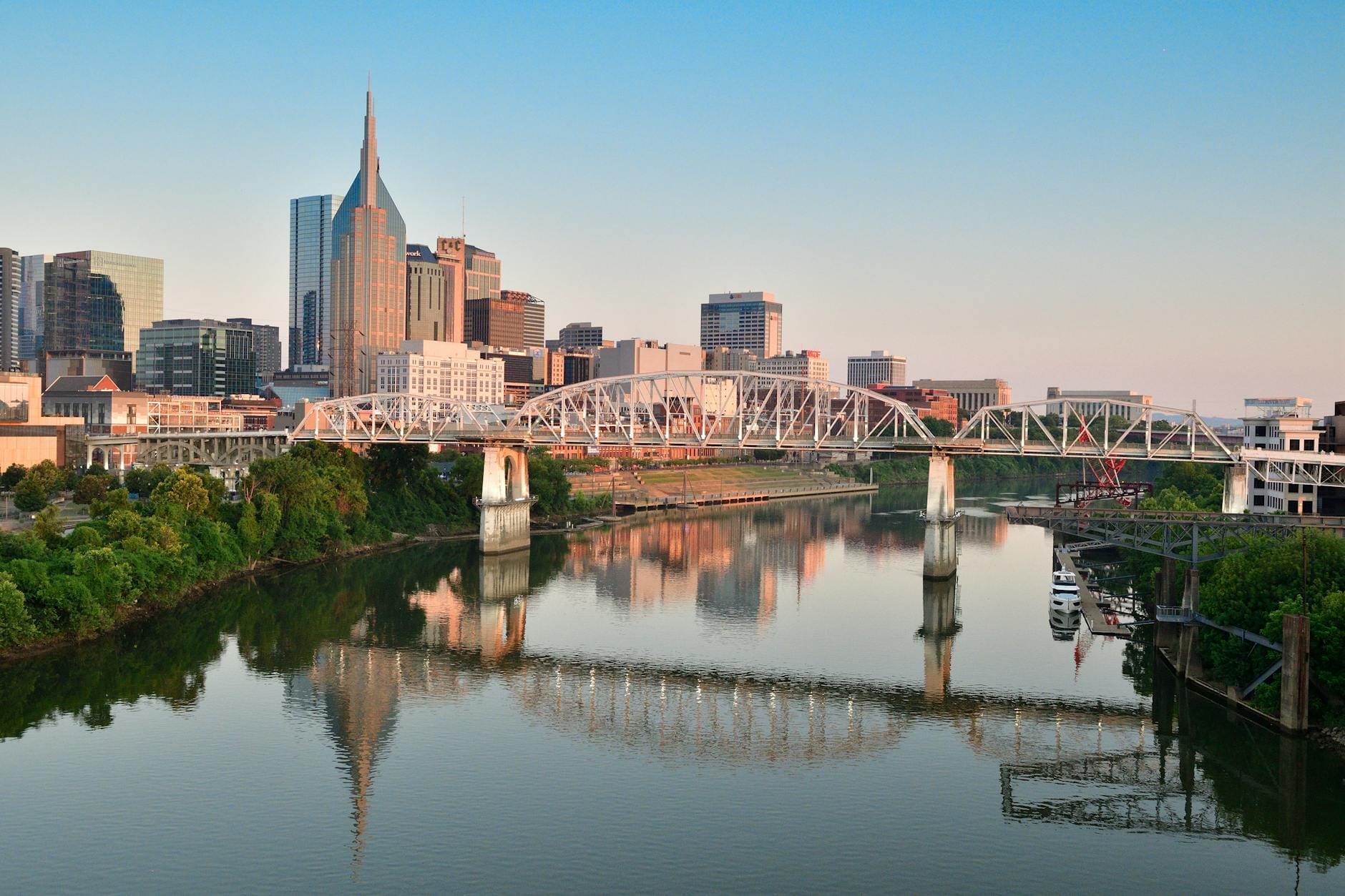 Vista panorámica del centro de Nashville con el río Cumberland y el puente peatonal John Seigenthaler en primer plano al amanecer.