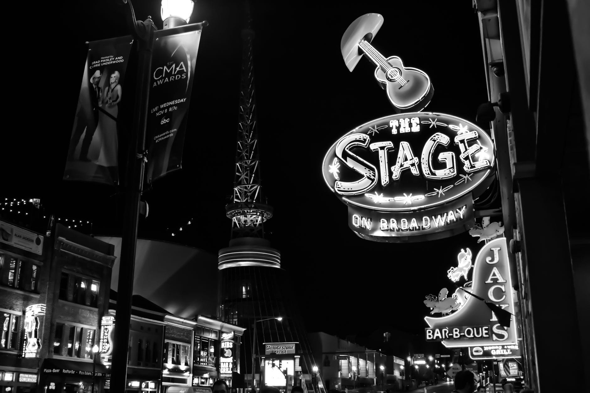 Foto en blanco y negro de Nashville Broadway de noche, con el letrero de neón del local de música en vivo The Stage y las luces de la ciudad.
