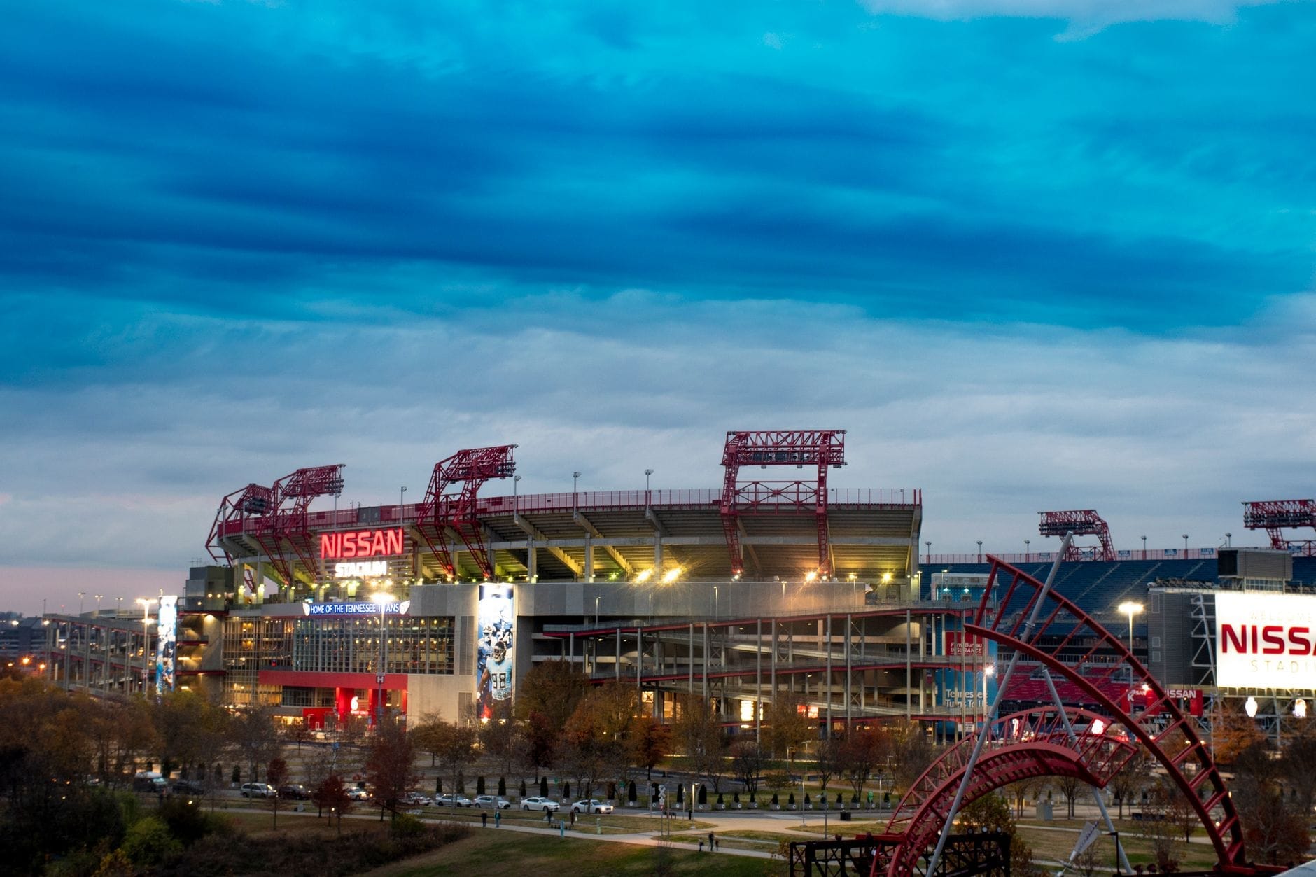Vista amplia del Nissan Stadium en Nashville bajo un cielo vespertino nublado, con luces brillantes del estadio e infraestructura visible para eventos al aire libre.