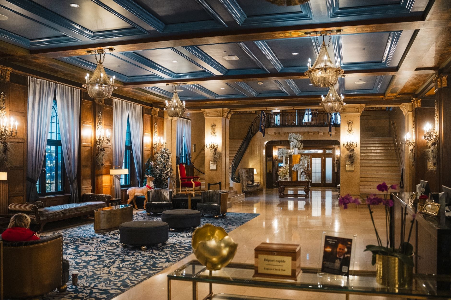 Lujoso lobby de hotel con elegantes lámparas de araña, techo azul, elaborados detalles en madera, cómodos asientos y una imponente escalera de bienvenida en Nashville.