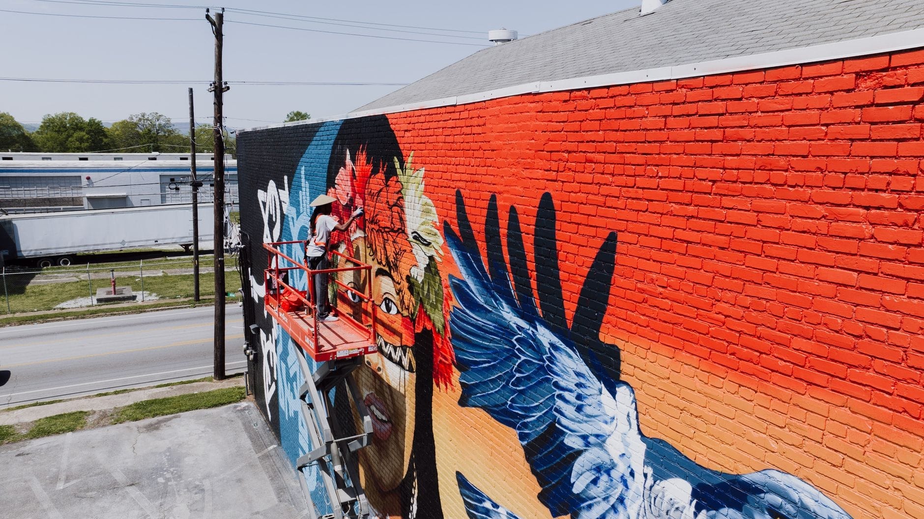 Mural brillante en progreso en una pared de ladrillo en Nashville, con una figura cantante de colores, plumas y elementos dinámicos azules y rojos.