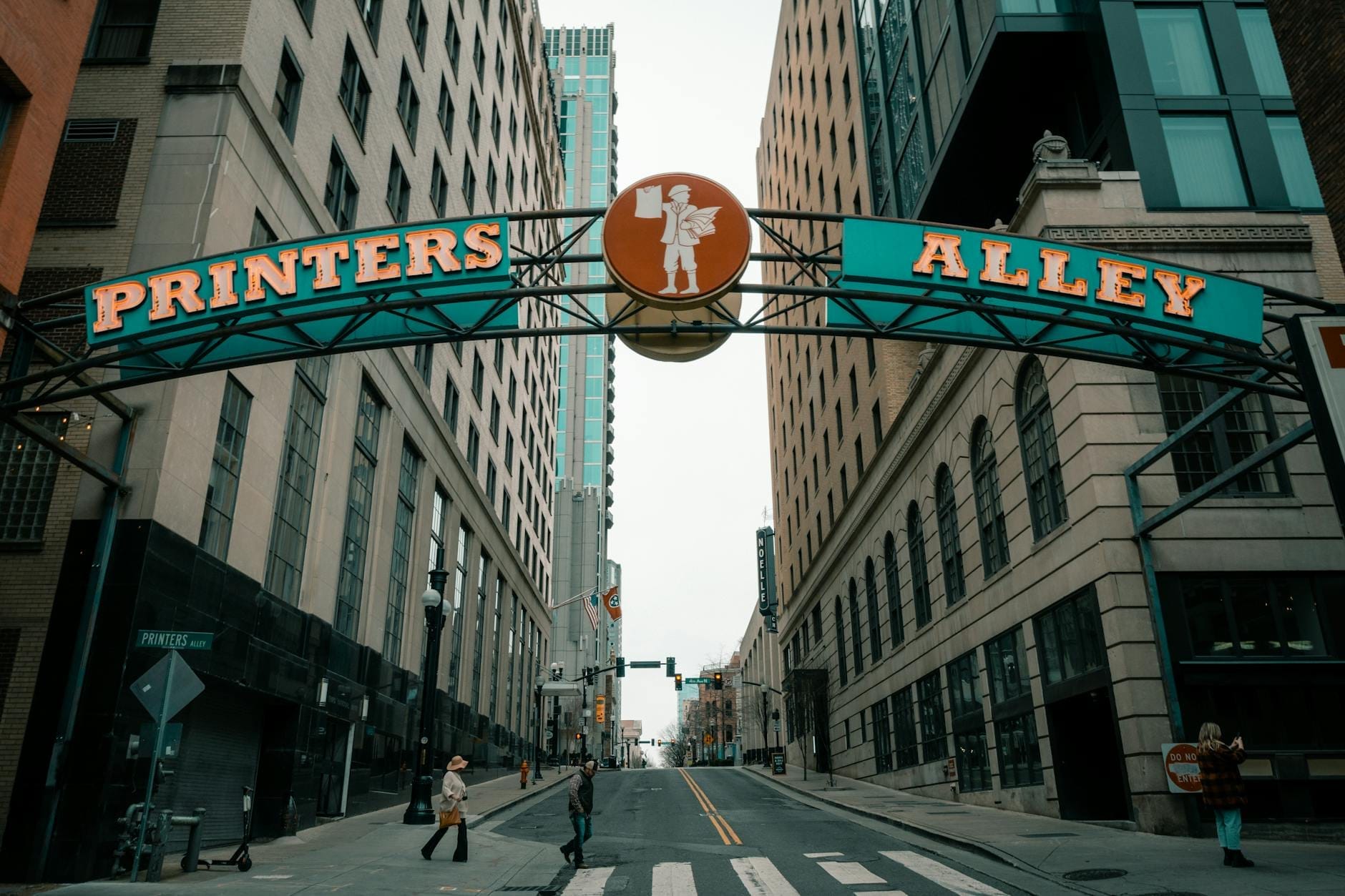 Vista de la calle Printer's Alley en Nashville con el icónico letrero en arco 'Printers Alley' entre edificios altos durante el día.