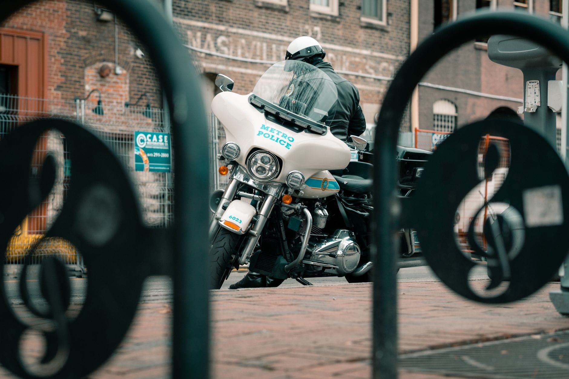 Oficial de policía de Metro Nashville en motocicleta estacionada frente a un edificio de ladrillo, visto a través de una barandilla en forma de nota musical.