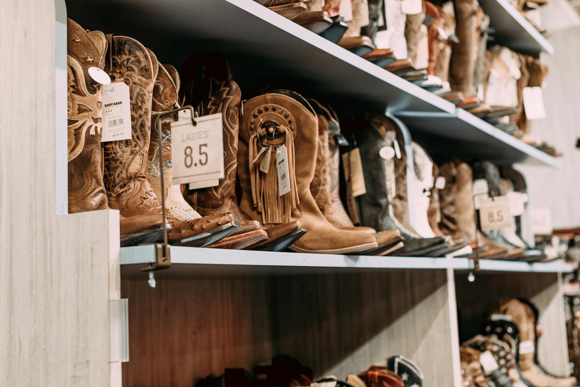 Estantes llenos de varios estilos de botas vaqueras en exhibición en una tienda de ropa western bien iluminada.