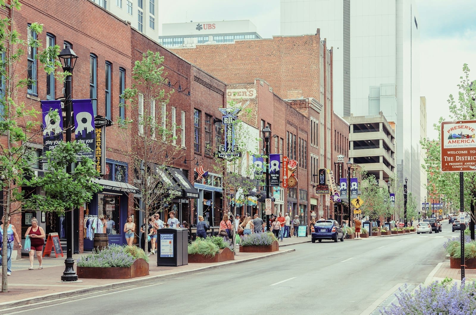 Calle animada en el centro de Nashville con edificios de ladrillo, tiendas, pancartas y personas caminando por las aceras durante el día.