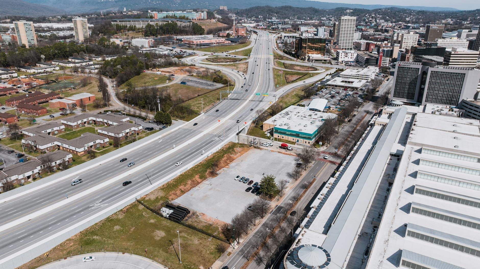 Vista aérea de una importante autopista interestatal con múltiples carriles que entran a la ciudad, rodeada de edificios urbanos y vegetación.
