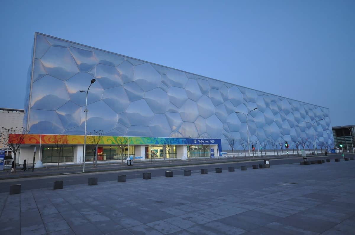 Weitwinkelansicht des Nationalen Aquatikzentrums von Beijing mit der ikonischen Blasenmuster-Fassade und dem bunten olympischen Eingangsbereich in der Abenddämmerung.