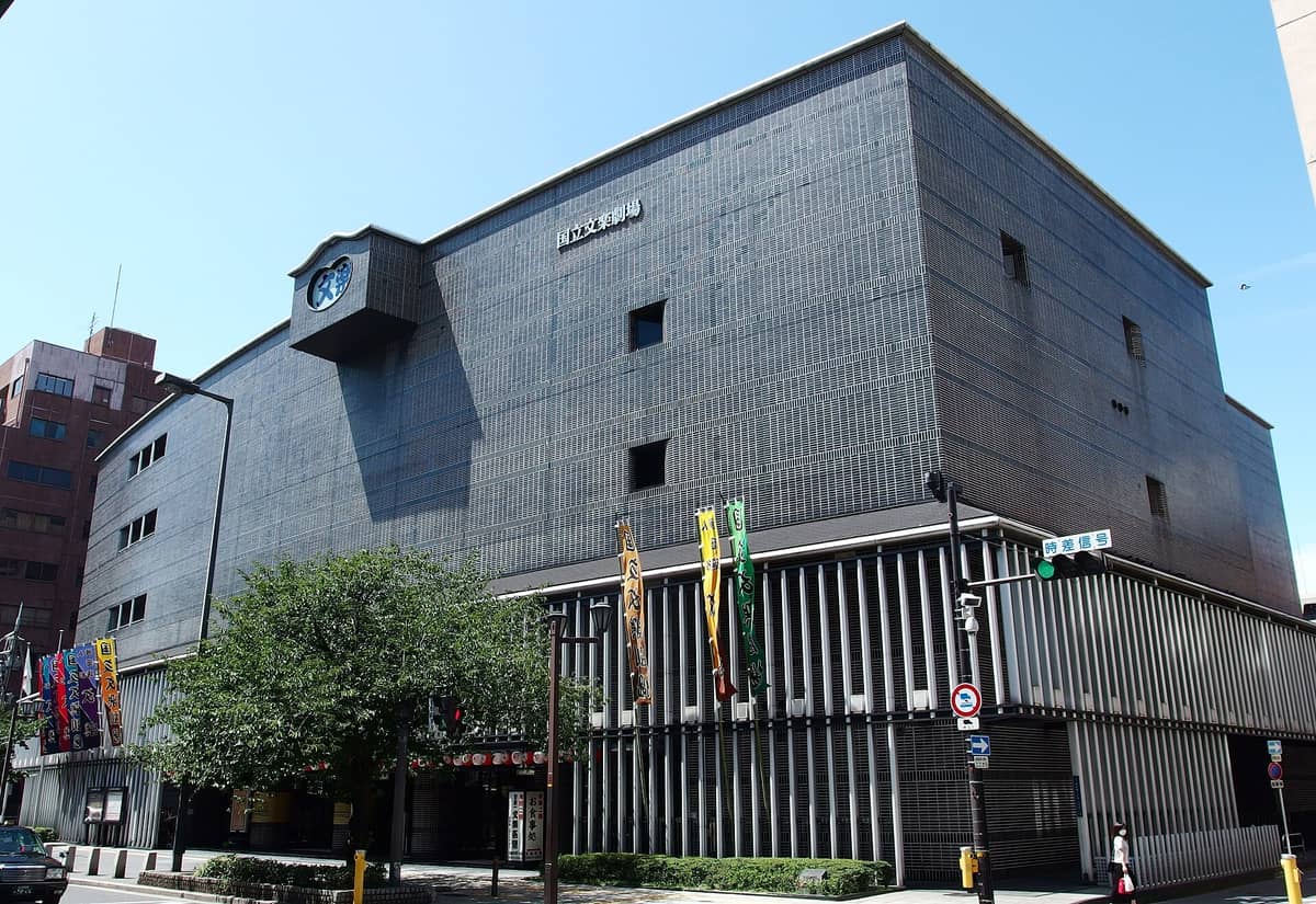 Exterior of the National Bunraku Theatre in Osaka viewed from the street, showing its distinctive modern facade with banners and signage.