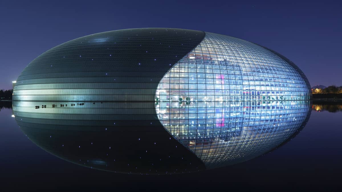 Das Nationale Zentrum für Darstellende Künste in Peking bei Nacht – die beleuchtete Titan-Glaskuppel spiegelt sich im umgebenden Wasser.
