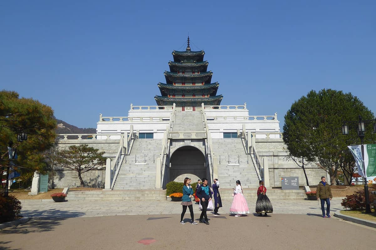 Vista frontal do Museu Nacional de Folclore da Coreia, com o icônico pagode de vários andares, escadarias de pedra e visitantes caminhando em primeiro plano.