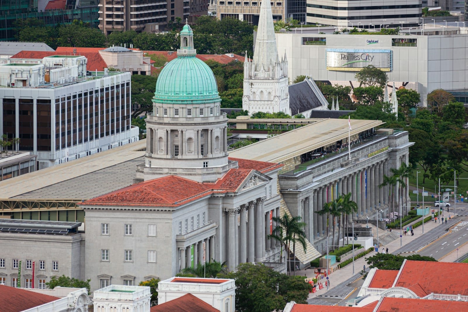 มุมมองทางอากาศของ National Gallery Singapore แสดงให้เห็นสถาปัตยกรรมอาณานิคมอันยิ่งใหญ่พร้อมโดมสีเขียว เสาคลาสสิก และอาคารต่างๆ ของเมืองโดยรอบ