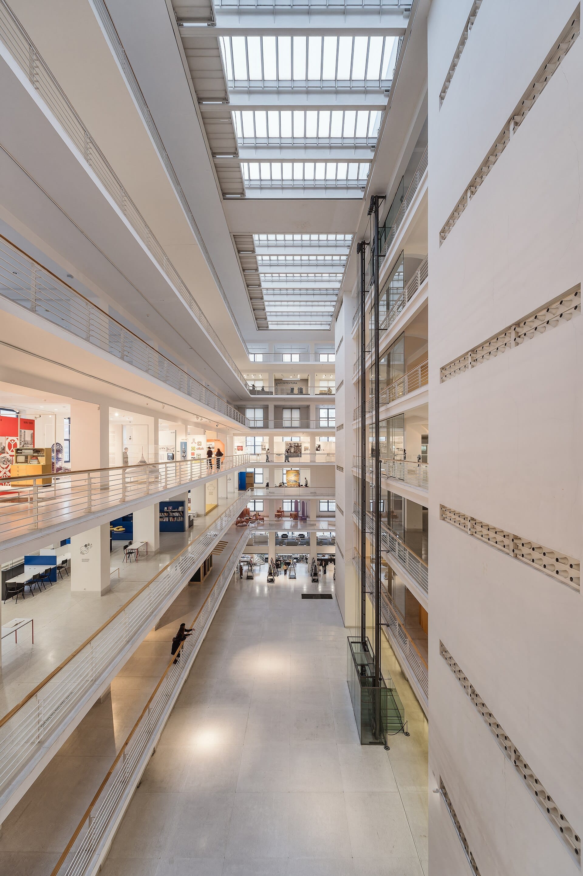 Przestronne, nasłonecznione atrium Veletržní Palace w Pradze, prezentujące wiele poziomów galerii z czystą, nowoczesną architekturą funkcjonalistyczną.