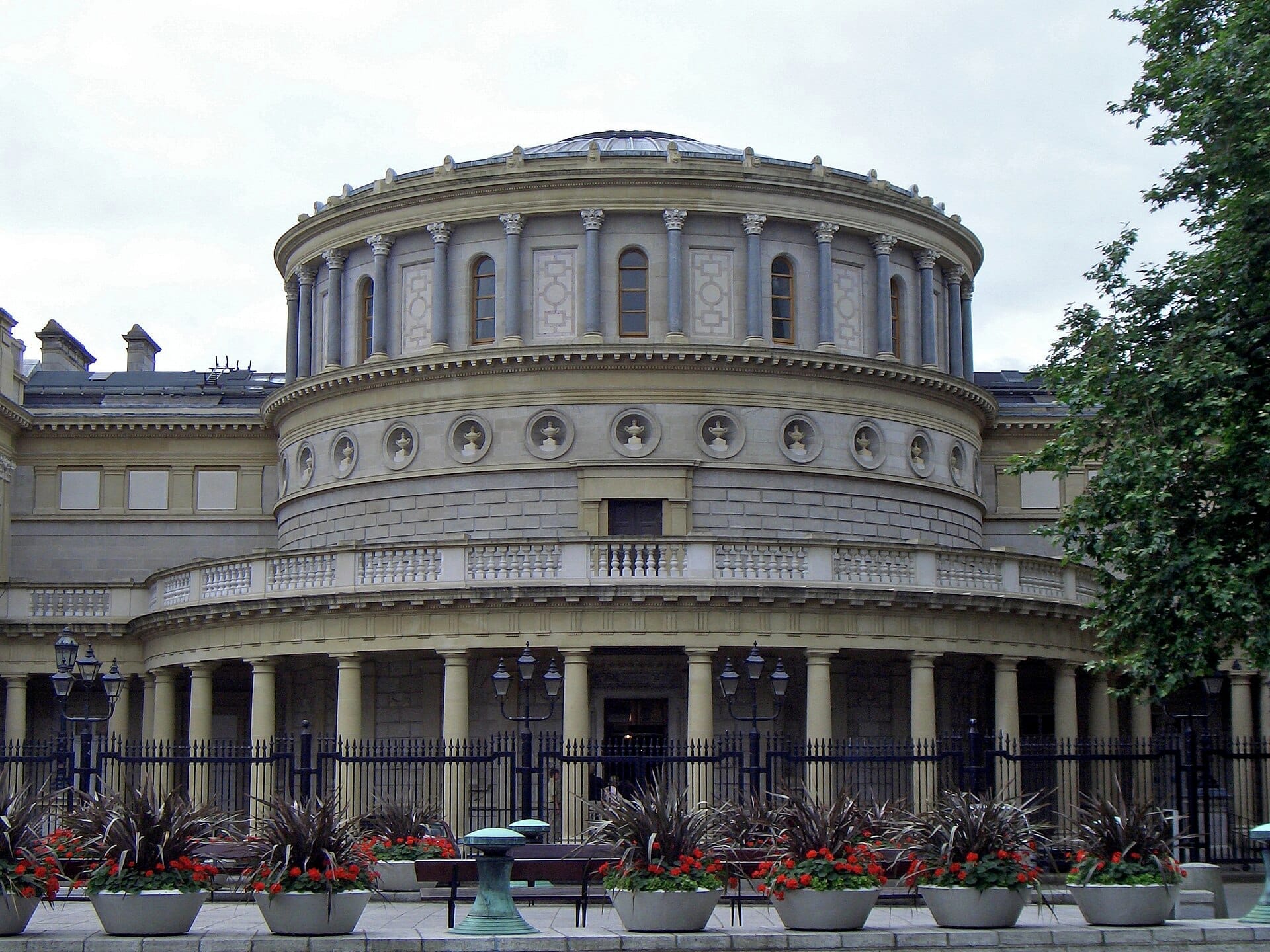 La grande rotonda e la facciata neoclassica del National Museum of Ireland – Archaeology, con colonne decorative, recinzione in ferro e vasi di fiori davanti.