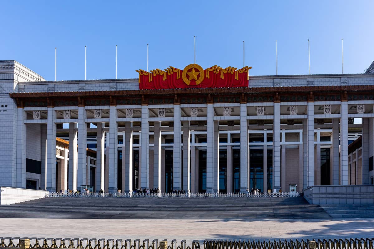 Weitwinkelaufnahme des Haupteingangs des Nationalmuseums von China mit hohen Säulen, breiten Treppenstufen und einem roten und goldenen Emblem über dem Eingang.