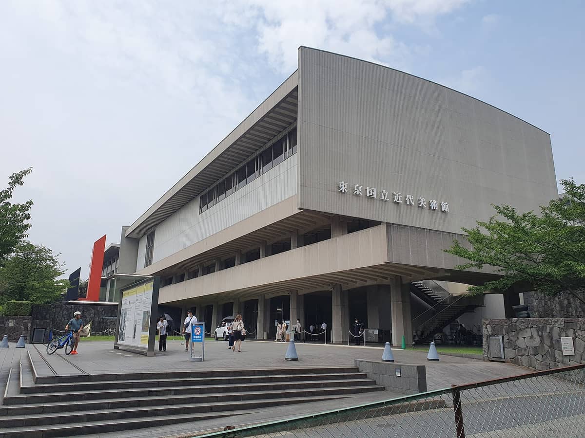 Facade of The National Museum of Modern Art, Tokyo with modern architecture, stairs, and a few visitors on a cloudy day.