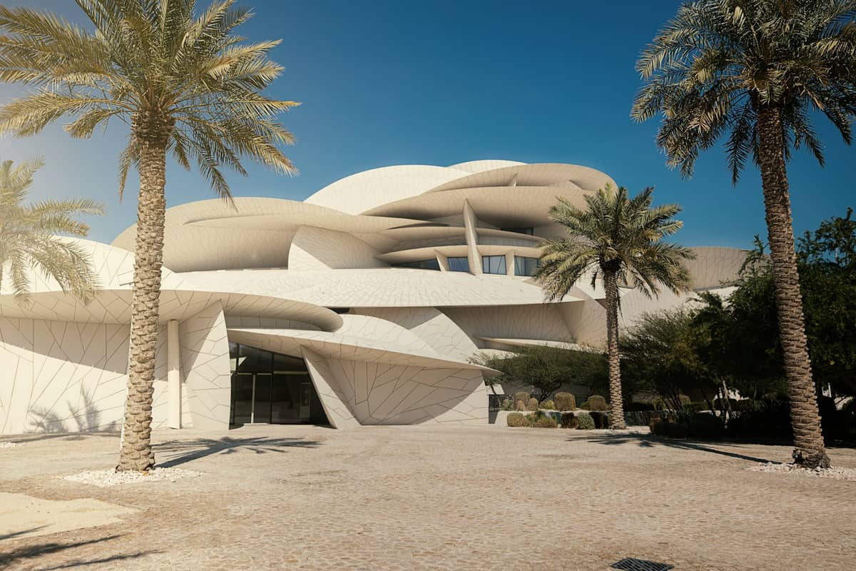 Außenansicht des Nationalmuseums von Katar mit seiner einzigartigen, ineinandergreifenden Scheibenarchitektur, gerahmt von Palmen und einem klaren Himmel.