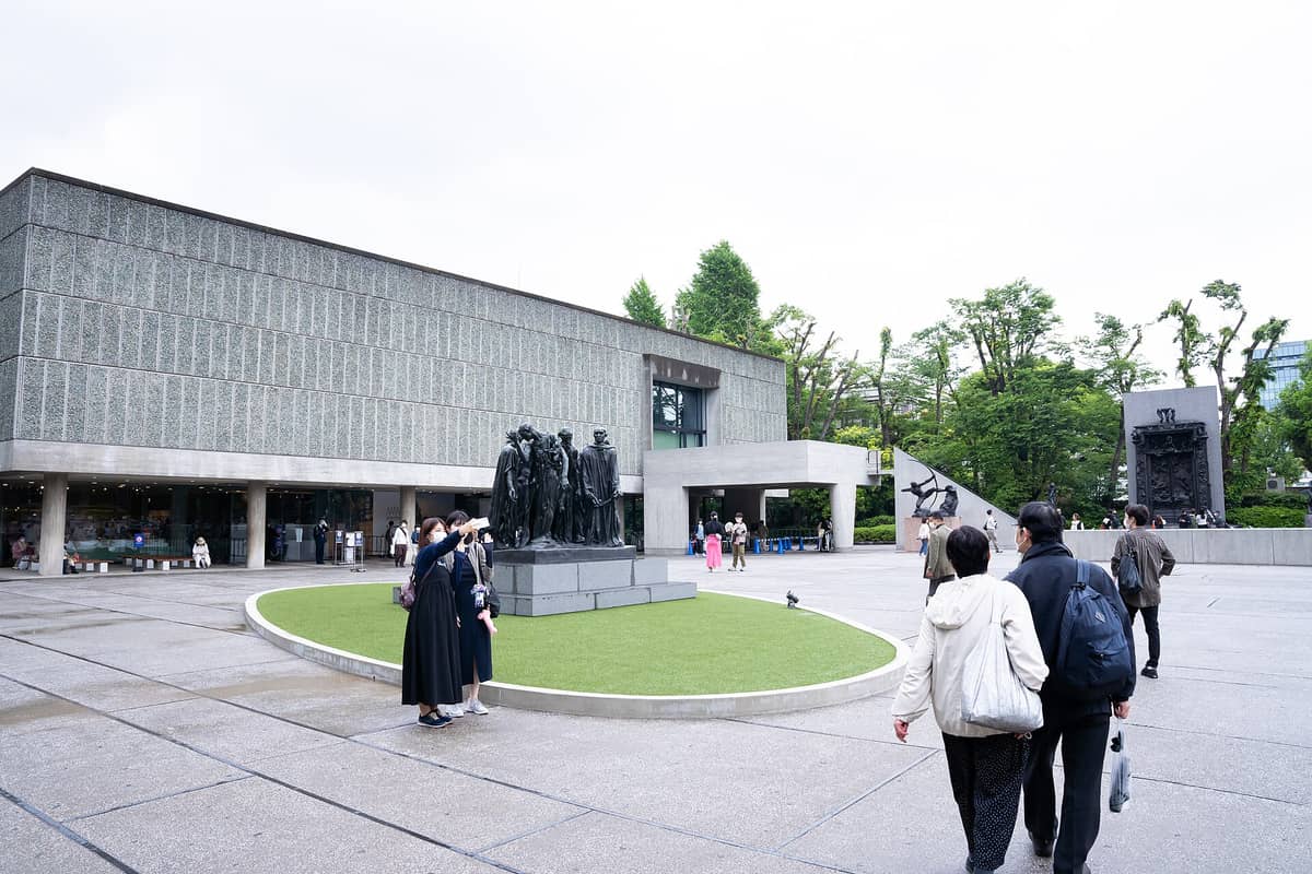 Wide view of the National Museum of Western Art in Tokyo, showing the modern Le Corbusier-designed facade, outdoor Rodin statues, and visitors in front of the entrance.