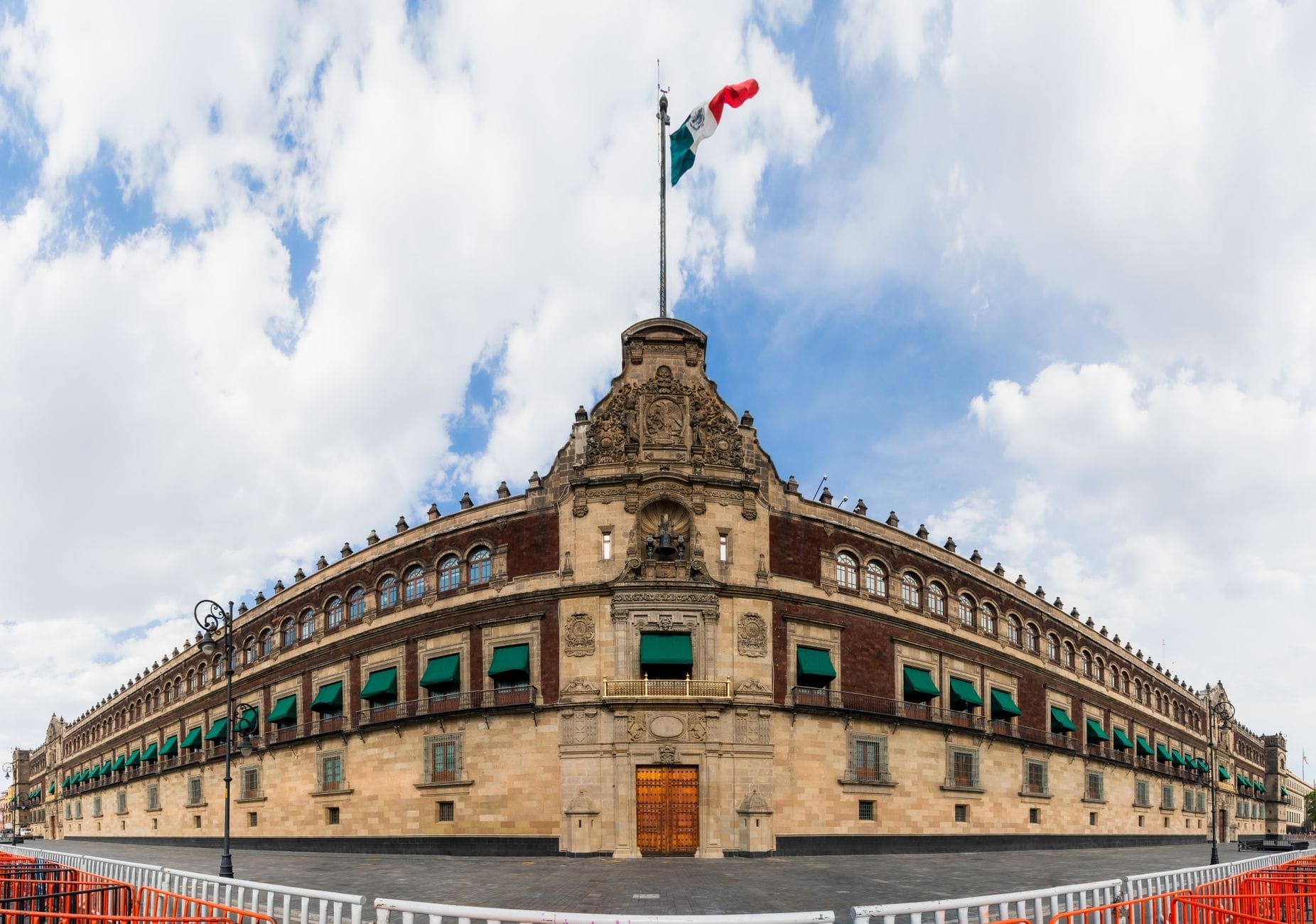 Vista panoramica del Palazzo Nazionale a Città del Messico con la bandiera messicana che sventola in alto, cielo nuvoloso e piazza deserta di fronte.