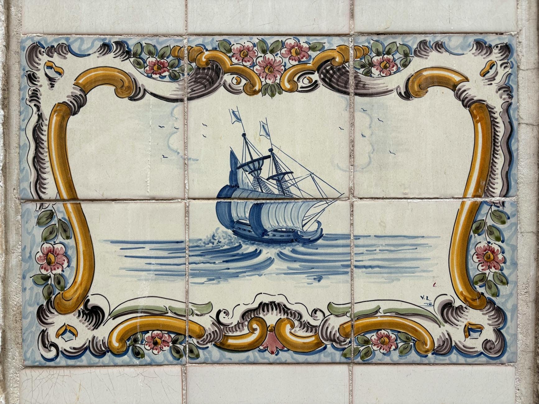 Primo piano di tradizionali azulejos portoghesi che raffigurano una nave blu incorniciata da elaborati motivi floreali gialli e rosa, espressione della maestria artigianale classica.