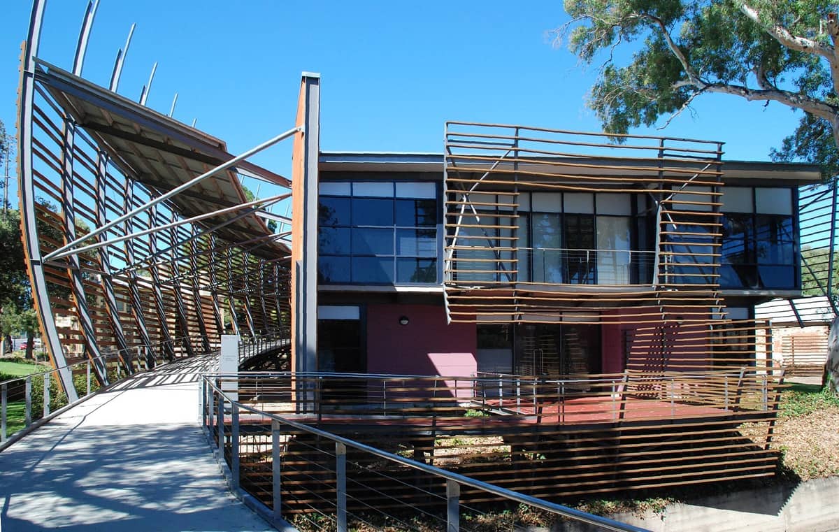 The National Wine Centre of Australia building with its modern glass facade, unique timber slats, and curved entrance under a bright blue sky.