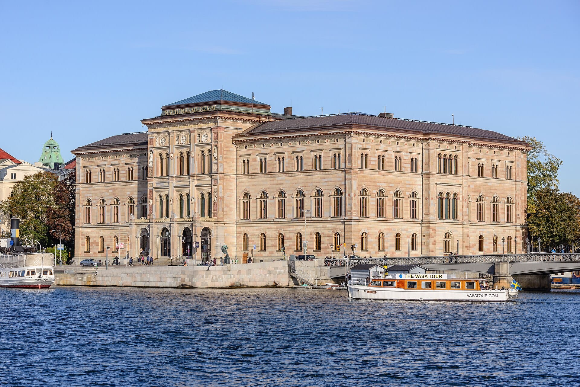 ด้านหน้าของ Nationalmuseum สตอกโฮล์ม มองจากฝั่งตรงข้ามแม่น้ำ ป้ายชื่อชัดเจน มีเรือท่องเที่ยวจอดอยู่ด้านหน้า