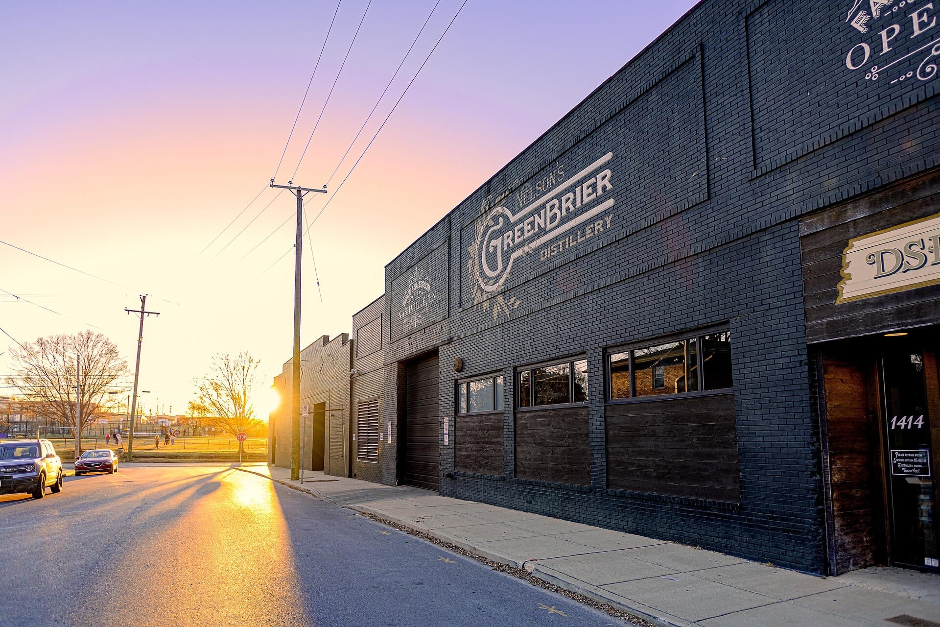 Exterior de Nelson's Green Brier Distillery en Nashville con fachada de ladrillo, gran letrero y luz de atardecer brillante en una calle tranquila.
